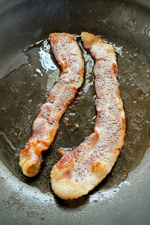 two strips of bacon sizzling in a skillet