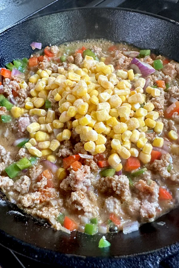 adding frozen corn to a skillet with ground meat and peppers