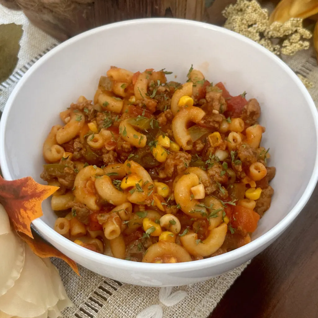 a bowl of goulash with elbow pasta, ground beef, corn, tomatoes and other vegetables.