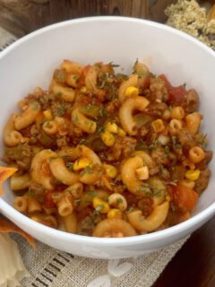 a bowl of goulash with elbow pasta, ground beef, corn, tomatoes and other vegetables.
