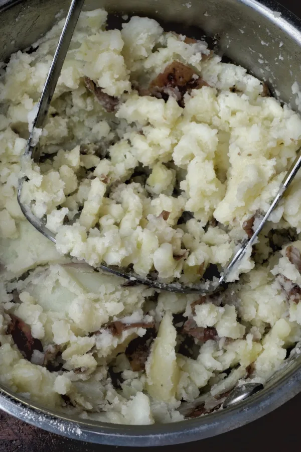 using a potato masher to mash red skin potatoes