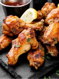 A plate of baked chicken wings with dipping sauce in the background.